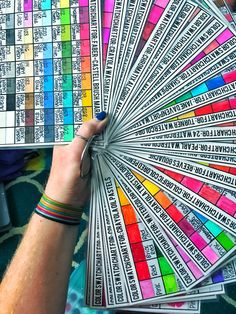 a person holding a fan with many different colors on it's sides and the words written in each section