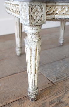 an old white table with wood flooring and flowers on the top, sitting on a hard wood floor