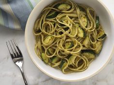 a white bowl filled with pasta and zucchini on top of a marble counter