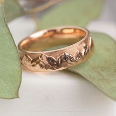 two gold wedding rings sitting on top of a green leafy branch with leaves in the background