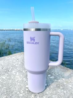 a purple tumbler cup sitting on top of a stone wall next to the ocean