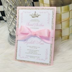 a pink and gold wedding card with a bow on it's front, sitting on a fur surface