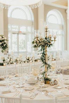 the tables are set up with white linens and gold candlestick centerpieces