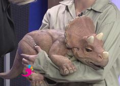 a woman holding a baby dinosaur in her arms while another person holds it behind her