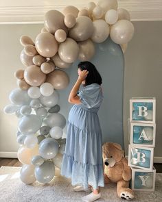 a woman in a blue dress standing next to balloons and a teddy bear on the floor