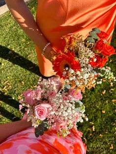 a woman in an orange dress holding a bouquet of red and white flowers on her arm