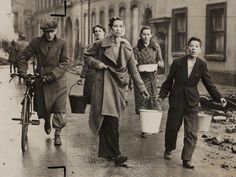 an old black and white photo of people walking down the street with buckets on their backs