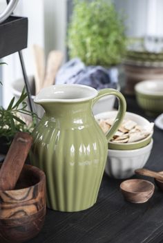 a green pitcher sitting on top of a wooden table next to bowls and spoons