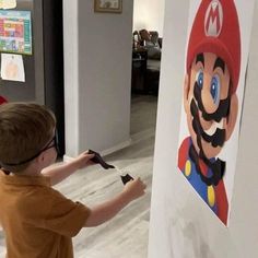 a young boy is painting a mario poster on the wall