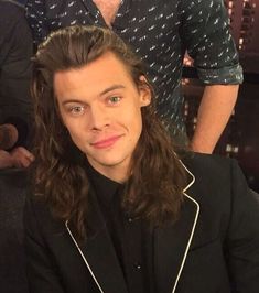 a young man with long hair sitting in front of another man wearing a black shirt