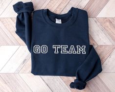 Get ready to cheer for your favorite team with our "Go Team" sweatshirt! This cozy crewneck features bold, high-quality embroidered lettering, perfect for game day, tailgates, or showing off your team spirit. Available in a variety of colors, this sweatshirt is made from a soft and durable cotton/polyester blend, offering comfort and warmth for any occasion. With unisex sizing available up to 5XL, it's a great fit for every sports fan. Material: Soft and durable cotton/polyester blend for ultima Embroidered Lettering, Team Sweatshirts, Go Team, Womens Hoodies, Gifts For Sports Fans, Comfort Design, Gameday Outfit, Sports Fan, Military Green