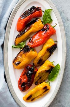 grilled peppers on a white plate with green leaves