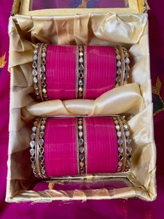 two pink bracelets are in a box on a purple cloth with gold trimming