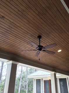 a ceiling fan mounted to the side of a wooden porch with two windows and shutters