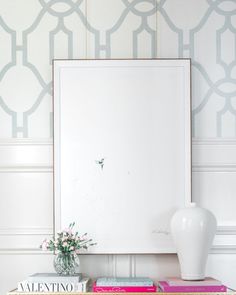 a white vase sitting on top of a table next to two books and a mirror