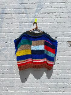 a multicolored sweater hanging on a white brick wall next to a green hook