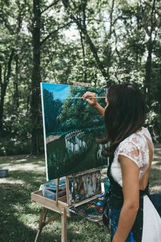 a woman is painting on an easel in the woods