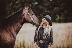 a woman wearing a cowboy hat standing next to a brown horse in a grassy field