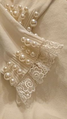 white lace and pearls are on top of a shirt that is rolled up in half