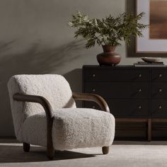 a white chair sitting in front of a dresser next to a potted plant on top of a table