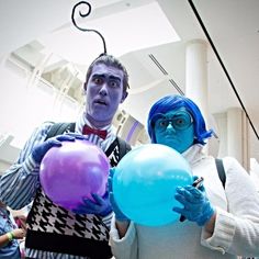 two people dressed in costumes holding balloons and wearing blue make up as they stand next to each other