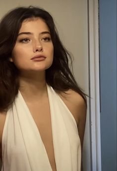 a woman with long hair wearing a white dress and looking at the camera while standing in front of a door