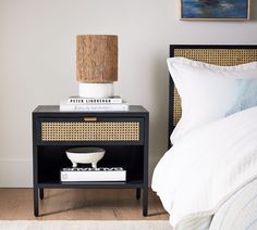 a nightstand with a lamp on top of it next to a bed