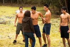 four shirtless men are standing around in the grass and looking at something on the ground