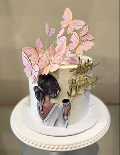 a white cake with pink flowers on top and a woman holding a coffee cup in front of it