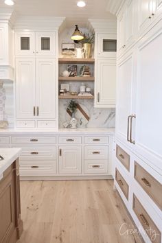 a kitchen with white cabinets and wood flooring in the center, along with marble counter tops