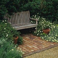 a wooden bench sitting in the middle of a garden filled with flowers and plants next to a brick walkway