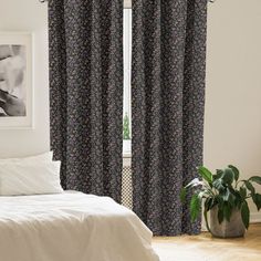 a white bed sitting next to a window covered in black and white floral print curtains