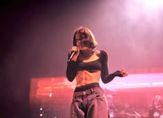 a woman standing on top of a stage holding a microphone in her hand and wearing high waisted jeans