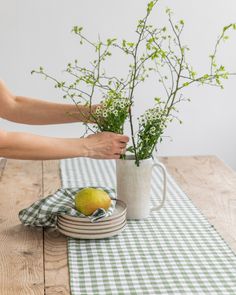 a woman is arranging flowers in a mug on a table with a green and white checkered cloth