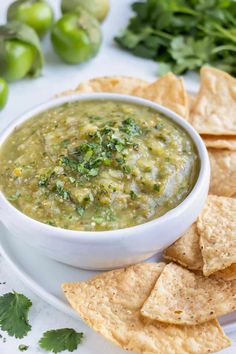 a white bowl filled with green salsa surrounded by tortilla chips