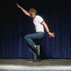 a man standing on top of a stool in front of a blue curtain with his arms out