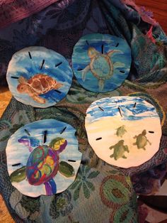 four painted plates with turtles and sea animals on them sitting on a cloth covered table