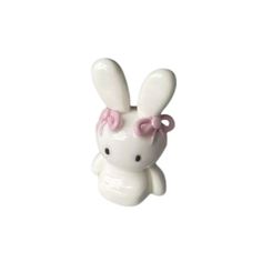 a small white bunny with pink bows on its head and ears, sitting against a white background