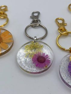 three different types of key chains with flowers in them on a white surface, one is yellow and the other is purple