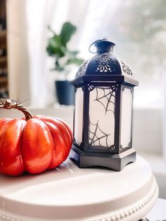 a lantern and two red pumpkins on a white table in front of a window