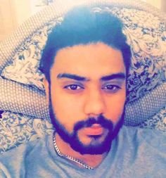 a man with a beard laying on a bed looking at the camera while wearing a t - shirt