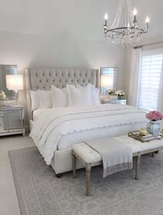 a bedroom with a large white bed, chandelier and two tables in front of it