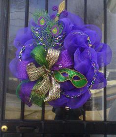 a purple and green wreath with a mask on it's front door, hanging from a metal gate