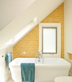 a white bath tub sitting next to a toilet in a bathroom under a slanted ceiling