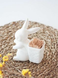 a white rabbit statue sitting next to a potted plant on top of a woven mat