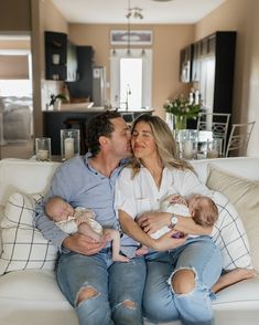 a man and woman are sitting on a couch with their two babys in their arms