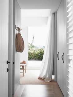 an open door leading to a white room with wooden flooring and curtains hanging from the ceiling