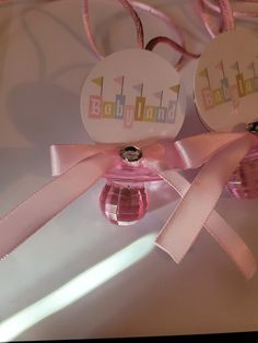 two tags attached to pink ribbon on top of a white table with balloons in the background