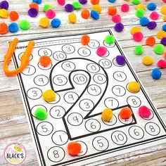 a number 2 coloring page with colored pom - poms on the floor and an orange marker next to it