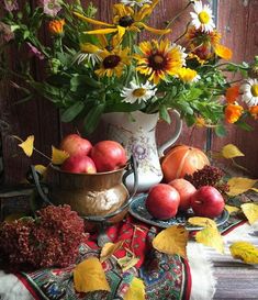 a vase filled with flowers and apples on top of a table next to other autumn decorations